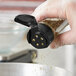 A hand using a 43/485 Black Flip and Sift spice lid to sprinkle seasoning into a container.