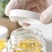 A hand holding a 53/400 white plastic lid over a clear jar.