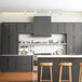 A Globe matte white industrial island light over a kitchen with grey cabinets and wooden stools.