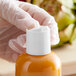 A person in gloves opening a white plastic bottle of orange liquid using a 28/410 white unlined disc top lid.