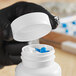 A person in black gloves holding a white child resistant cap on a white bottle of blue pills.