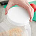 A hand holding a 110/400 unlined white plastic cap over a plastic container.