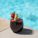 A Tossware plastic vino glass of red liquid with strawberries and lime wedges on the edge of a pool.