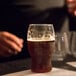 A Tossware plastic pint glass of dark beer on a table.