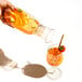 A person pouring fruit drink from a Tossware carafe into a glass of fruit.