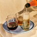 A person pouring red wine into two Tossware Reserve stemless wine glasses on a tray.