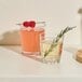 Two Tossware rocks glasses filled with liquid on a table with a rosemary sprig.