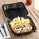 A sandwich and chips in a Genpak black plastic container.