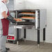 A man wearing a face mask and gloves holding a tray of bread in a Cooking Performance Group electric convection oven.