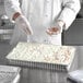 A person in a white coat sprinkles sprinkles on a frosted cake in a Baker's Lane foil cake pan.