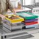 A person in a chef's uniform using green Pan Stacker trays to hold food in stainless steel hotel pans.