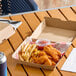 A corrugated clamshell container filled with fried chicken tenders, French fries, and a cup of dipping sauce.