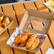 A small corrugated clamshell container with a clear window, holding several pieces of fried chicken tenders.