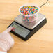 a hand touching a container of sprinkles on a scale