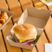 A cheeseburger with lettuce, tomato, and onion in a 4 x 4 x 3 inch corrugated clamshell container.
