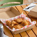 A brown corrugated clamshell container holding fried chicken pieces, lined with red and white checkered paper.