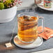 A glass mug of Dona Honey Herbal Tea with a tea bag in it.