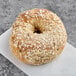 A Just Bagels multigrain bagel with oats on top on a white surface.