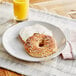 A multigrain Just Bagels bagel on a plate with cream cheese and orange juice.