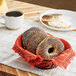 Just Bagels Authentic New York Poppy Seed Bagels in a basket on a table next to a cup of coffee.