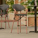 A Lancaster Table & Seating brown Teslin outdoor arm barstool on an outdoor patio.