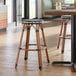 A backless barstool with a black and white checkered weave seat and rattan-style legs.