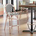 A black and white woven rattan outdoor side barstool with a wooden frame and curved backrest.