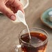 A hand holding a plastic cup of coffee with Nestle Coffee-Mate French Vanilla being poured into it.