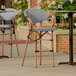 Two Lancaster Table & Seating black and white outdoor arm bar stools on a patio.