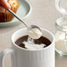 A spoonful of Nestle Coffee-Mate powder being poured into a mug of coffee.