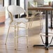A light wood and gray outdoor arm barstool with a curved back and woven seat.