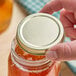 A hand holding a jar of honey with a gold metal lid.