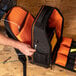 A person holding an orange and black Klein Tools backpack with a device inside.