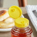 A plastic container with a yellow lid on a jar of honey.