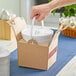 A hand placing a white Sabert Soup-N-Serve container in a cardboard box.