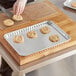 A hand in gloves cutting cookies on a Baker's Lane foil cookie sheet.