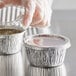 A person's hand in a plastic glove putting a lid on a small round aluminum container.