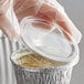 A person in gloves using a Baker's Lane plastic lid to cover a small clear plastic container.