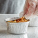 A close-up of food in a round foil ramekin with a board lid.