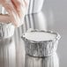 A hand in a plastic glove placing a white lid on a round aluminum Baker's Lane foil container.