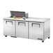 A True commercial stainless steel refrigerated sandwich prep table with 3 doors and food on top.