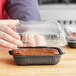 A person holding a Solut clear plastic lid over a brownie in a black container.