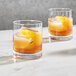Two Della Luce rocks glasses with ice and orange liquid on a table.