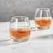 Two Della Luce Avalon Rocks glasses filled with brown liquid on a marble surface.