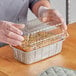 A person in gloves holding a Baker's Lane aluminum foil loaf pan filled with food.