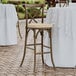 A Lancaster Table & Seating outdoor cross back bar stool with a tan cushion on the seat.