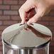 A hand holding a stainless steel lid with a chrome handle.