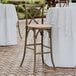 A Lancaster Table & Seating Vineyard Series Whiskey Brown outdoor cross back bar stool with a Chardonnay tan linen cushion on a patio table.