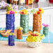 A collection of colorful Acopa green ceramic tiki mugs filled with fruit on a counter.