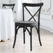 A black Lancaster Table & Seating outdoor cross back chair with a peppery black cushion next to a white table in a restaurant.